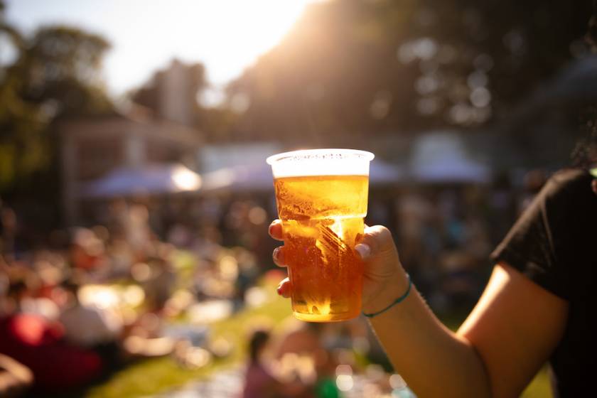 Person holding cup of beer outside with blurry background of a festival